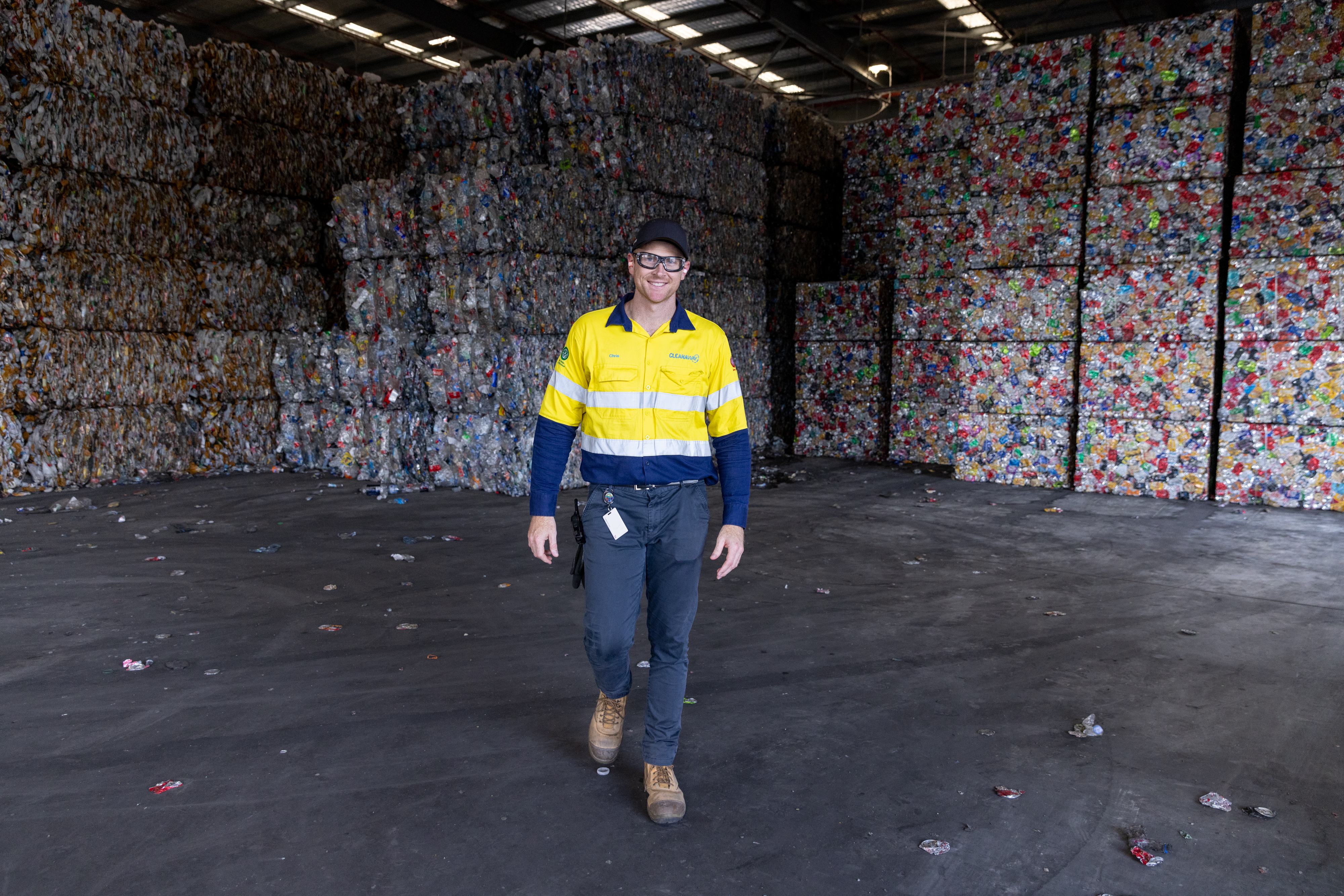 Man walking towards camera in PPE in front of container bales