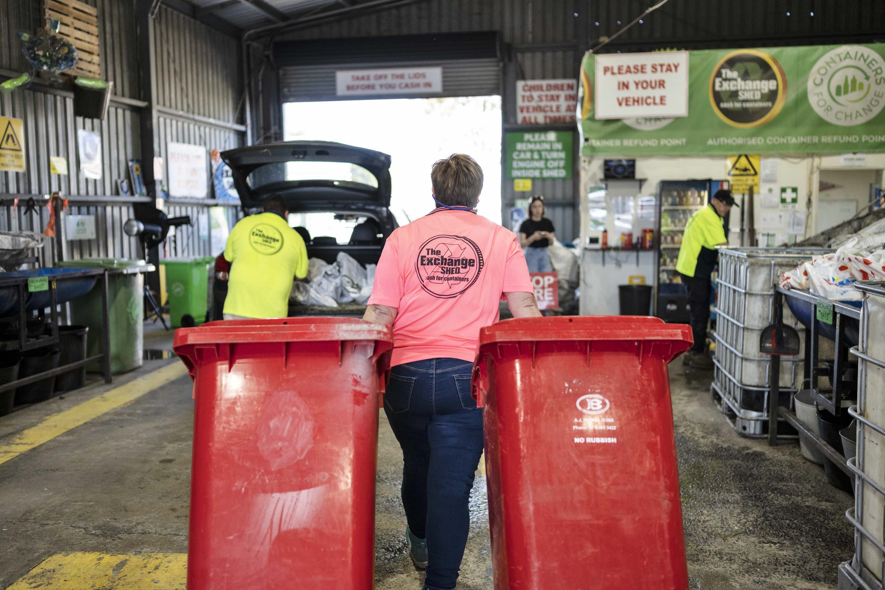 Woman in pink shirt dragging wheeling bins