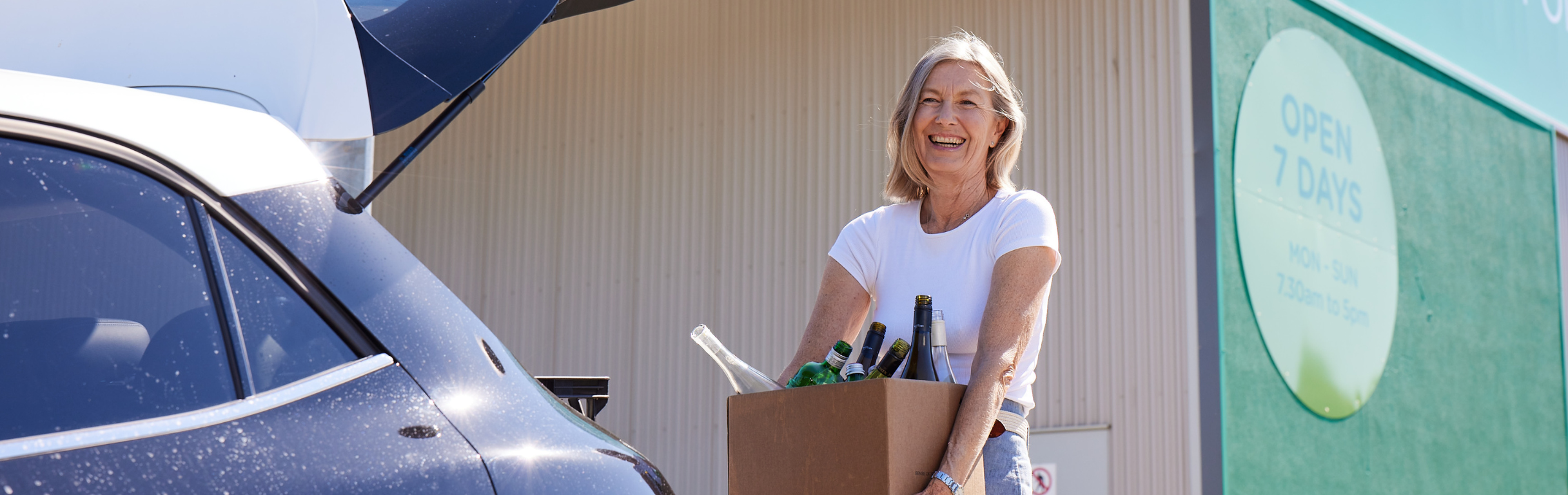 Woman holding box of containers after unloading from car boot at refund point