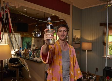 Young man holding up empty sports drink bottle after a party with streamers
