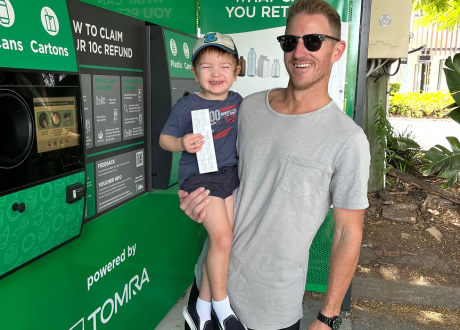 Father and son smiling after refunding their empty bottles and cans at a reverse vending machine