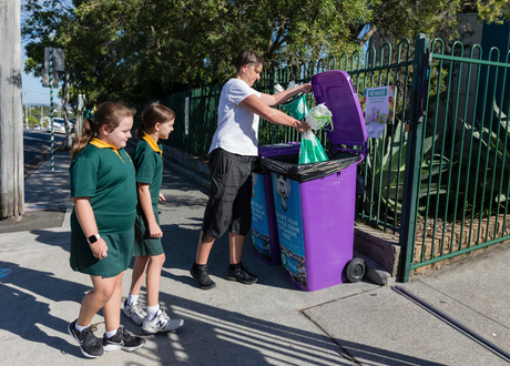Woman places bag in purple bin while kids watch on