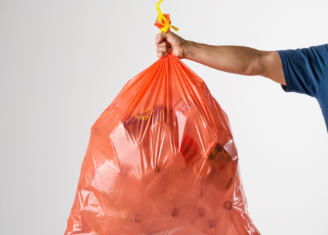 Person holding a plastic garbage bag full of empty drink bottles and cans