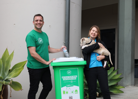 Man, woman and puppy standing in front of green recycling bin