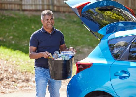 Man holding tub of containers in front of car