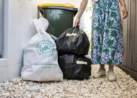 Person placing bags of containers beside recycling bin